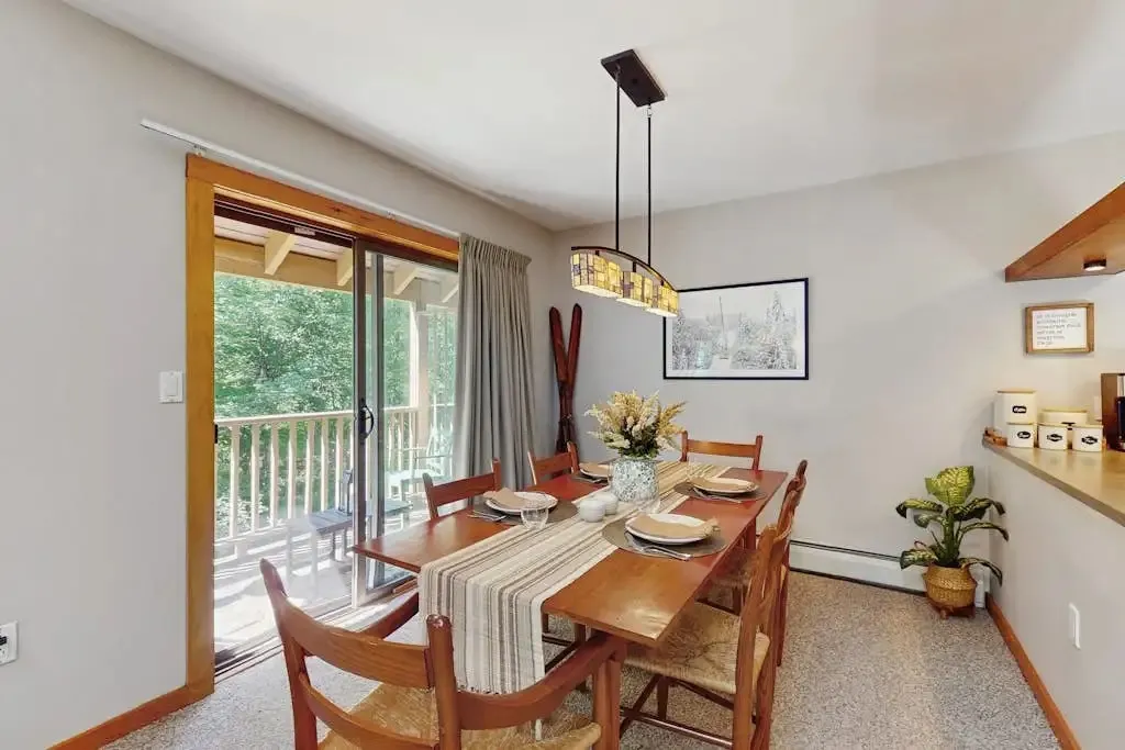Dining area with a wooden table set for six beside a sliding glass door to the balcony