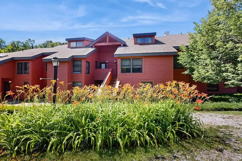 Red-sided condo building exterior in summer with blooming daylilies in front