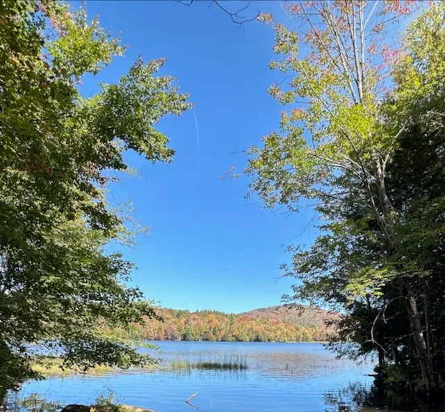 Calm blue pond ringed by maples, with colorful foliage on the far shore