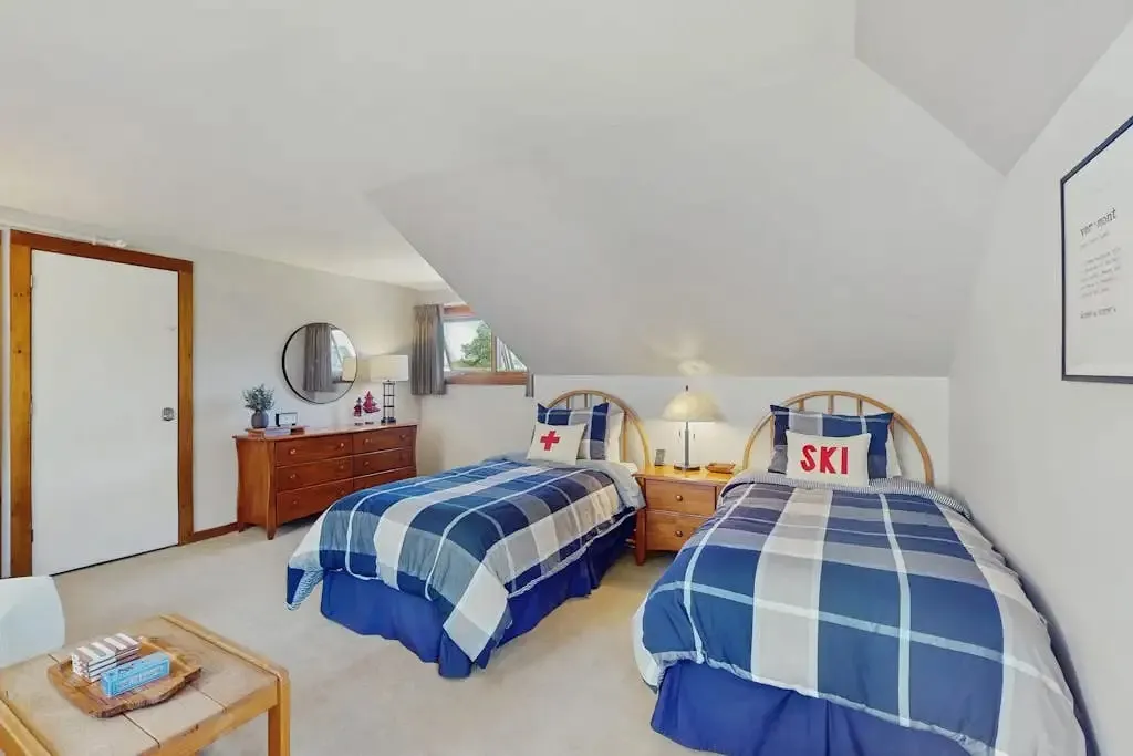 Loft bedroom with twin beds, a round mirror over a dresser, and a small seating nook