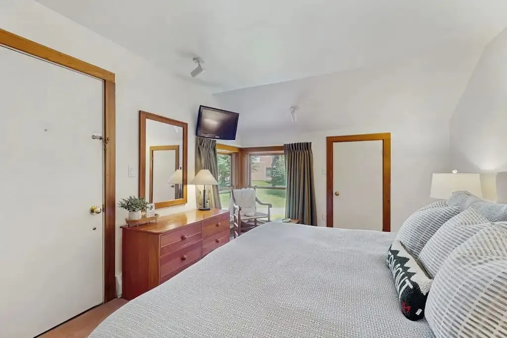 Primary bedroom with a dresser and mirror, wall-mounted TV, and a chair by the window