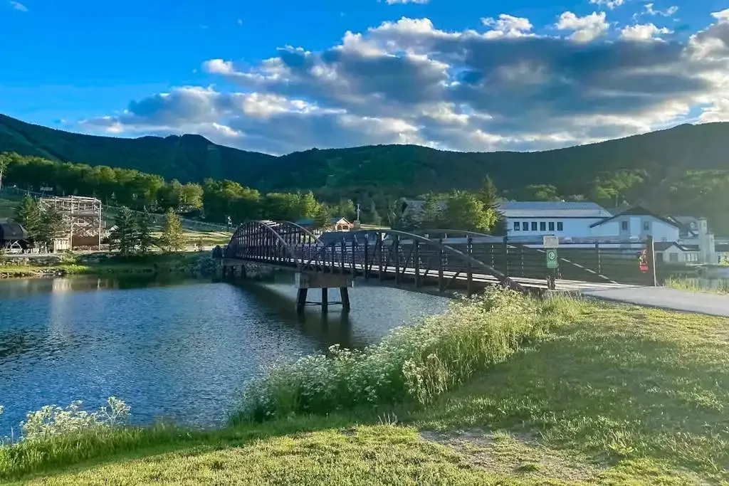 Footbridge over a pond with mountains and resort buildings in the background