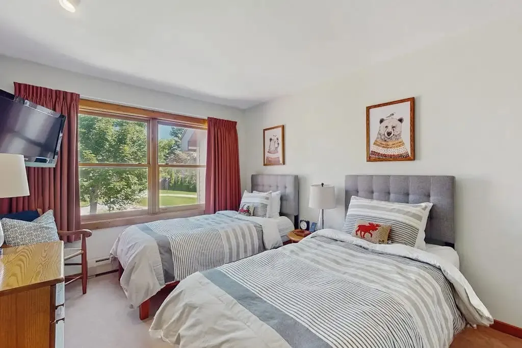 Wide view of the second bedroom with twin beds, a wood dresser, and a window overlooking the grounds